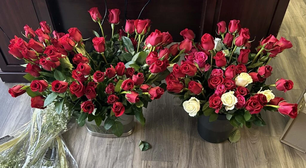 Multiple arrangements of red and white roses sit on the floor in vases, creating a vibrant display prepared for a special occasion.