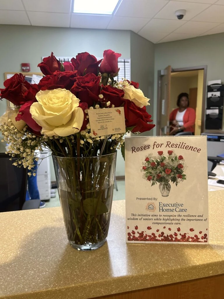A bouquet of red and white roses sits on a reception counter beside a sign reading “Roses for Resilience” presented by Executive Home Care.