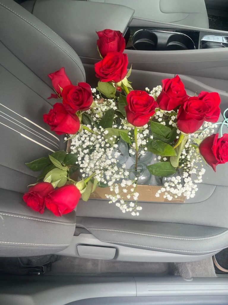 Several red roses arranged with baby’s breath sit in small vases placed on a car seat.